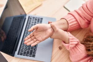 A person experiencing discomfort while working at a laptop, possibly due to carpal tunnel syndrome. Learn what is carpal tunnel and how to manage it.