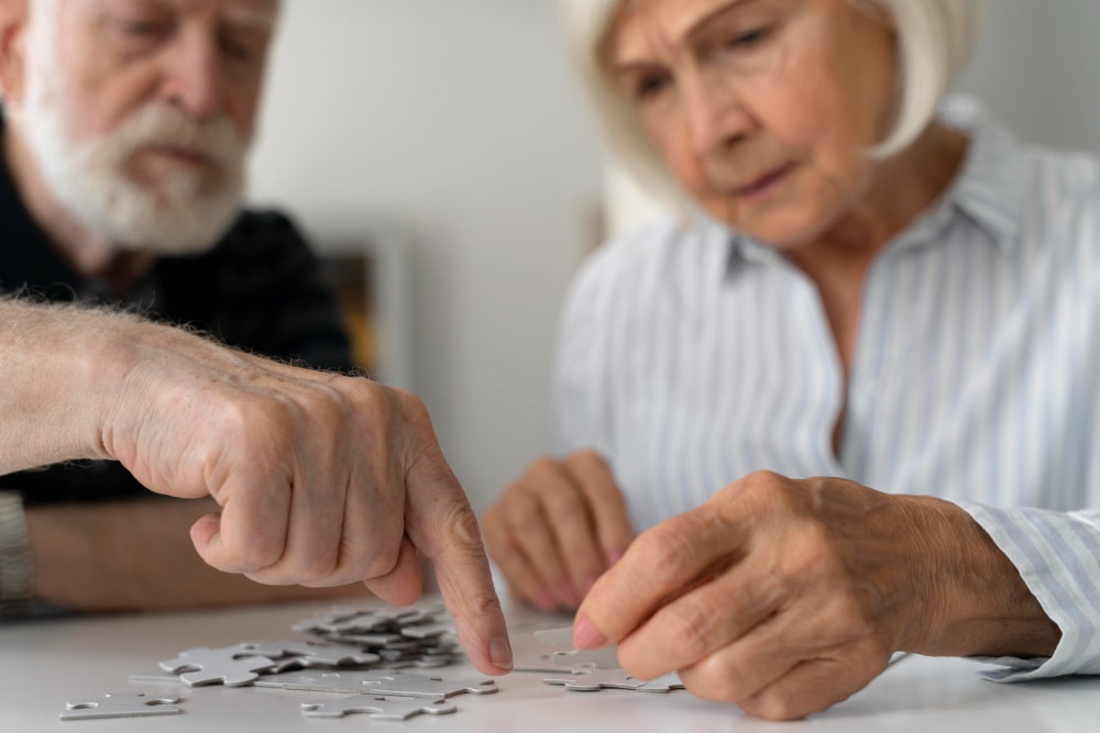 Elderly couple working together on a puzzle, illustrating cognitive challenges related to the 7 stages of Alzheimer's chart.