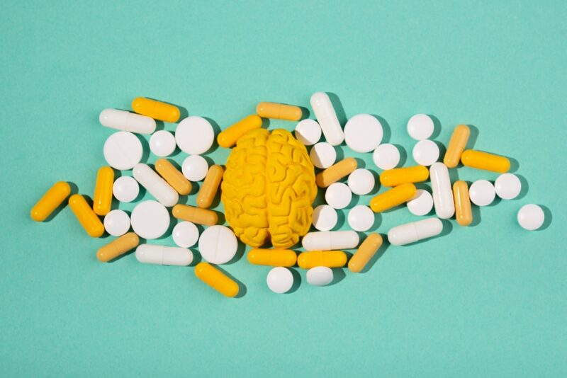 A yellow brain model surrounded by various pills, symbolizing the link between vitamin D deficiency neurological symptoms and brain health.